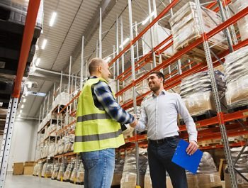 wholesale, logistic, people and export concept - manual worker and businessmen with clipboard shaking hands and making deal at warehouse
